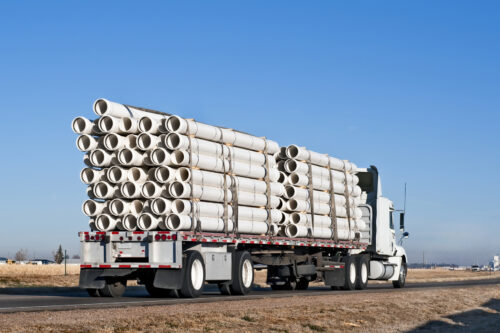 Big truck with flatbed trailer hauling plastic pipe.